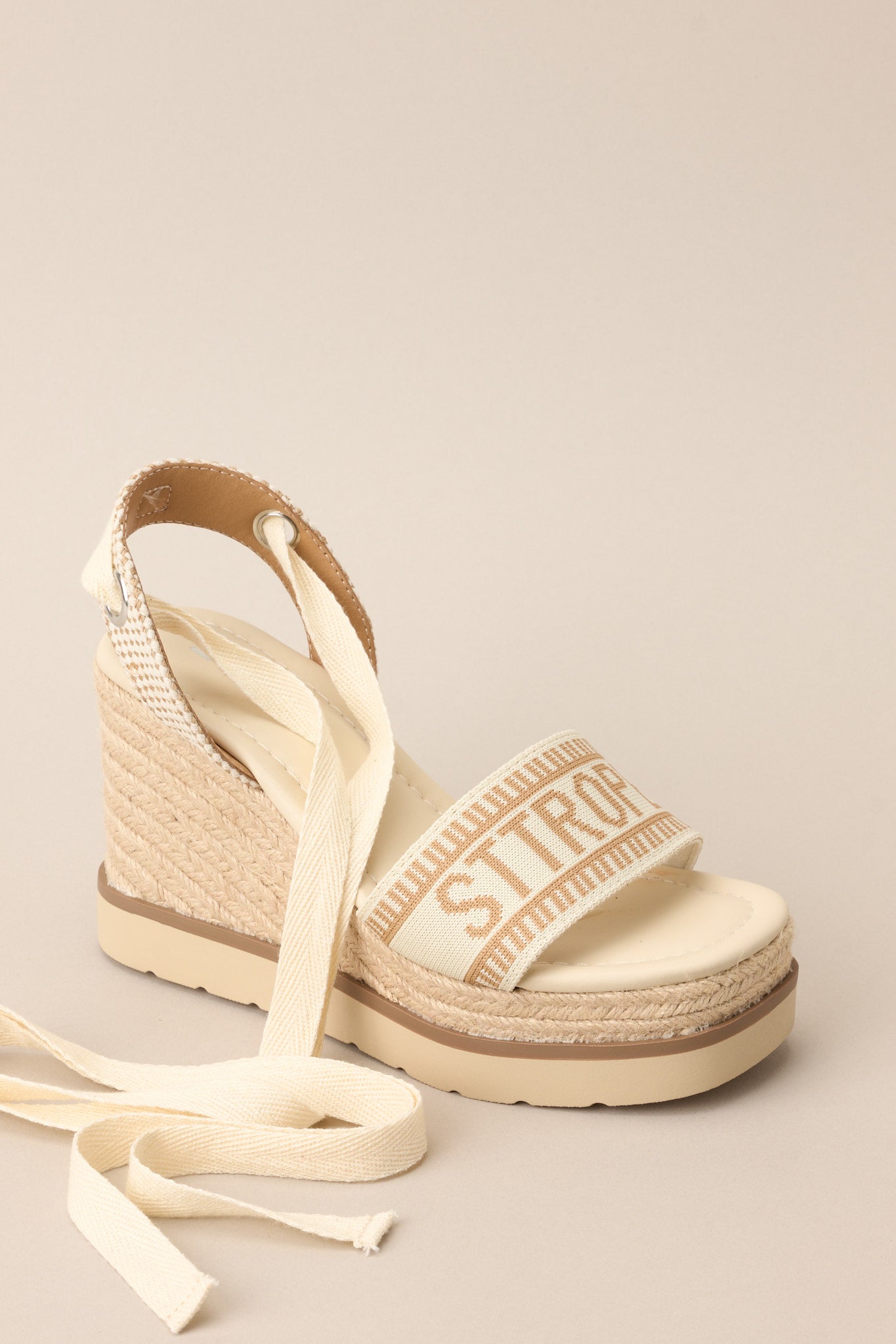 Angled side view of these sandals that feature a rounded toe, a strap over the top of the foot and around the heel, adjustable self-tie straps around the ankle, and a wedged heel.