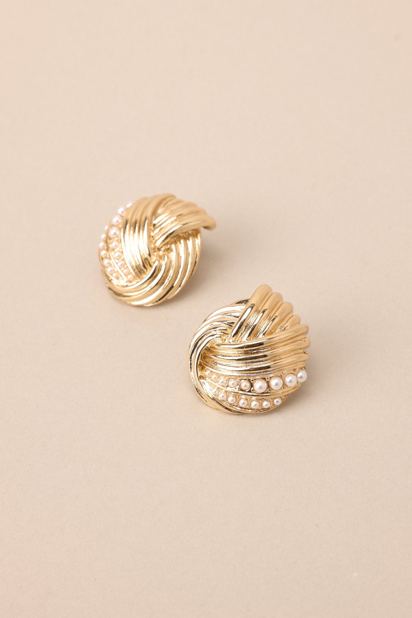 Close up view of these gold earrings with intertwined design and small faux pearl detailing, secure post backings.