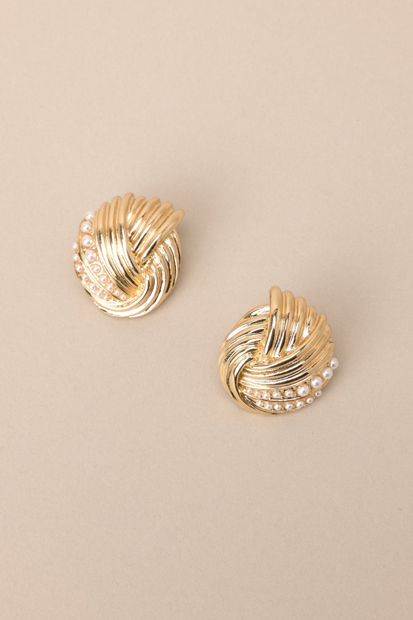 Overhead view of these gold earrings with intertwined design and small faux pearl detailing, secure post backings.