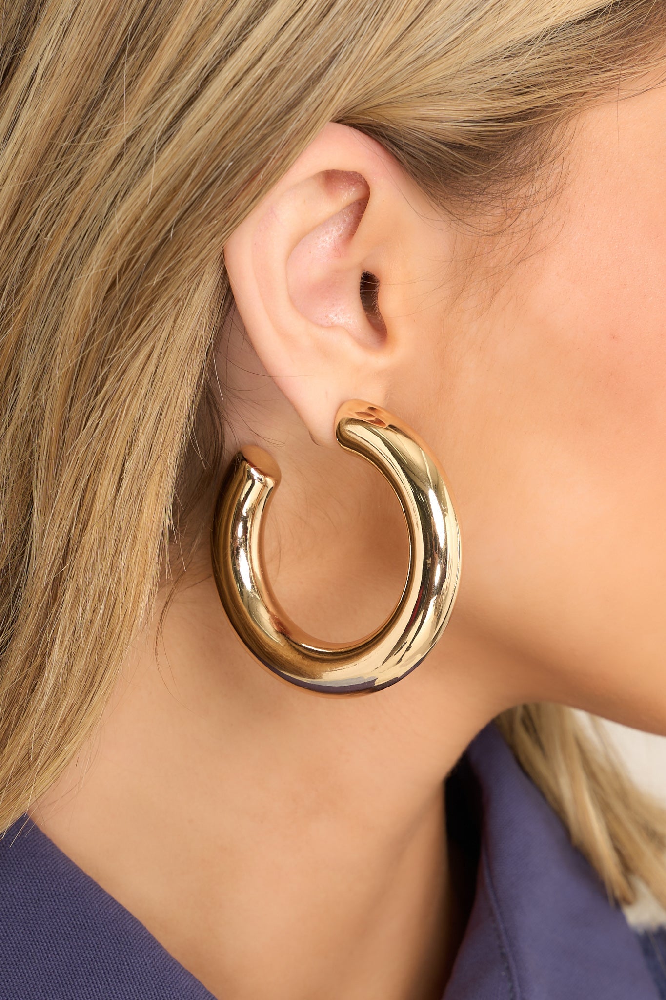 Close-up of a large gold hoop earring with an open circular design. The earring features a smooth, polished surface that reflects light.