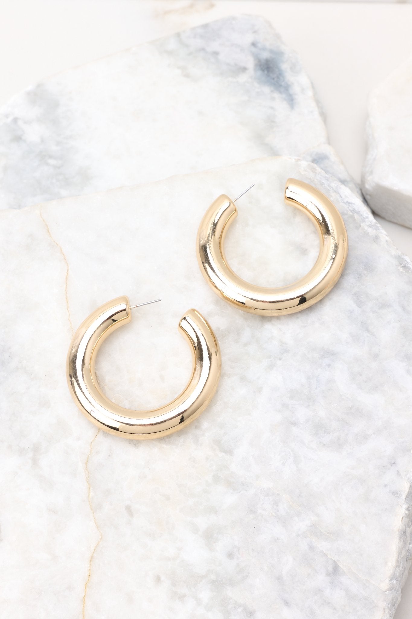 Overhead View of a pair of large gold hoop earrings with an open circular design. 