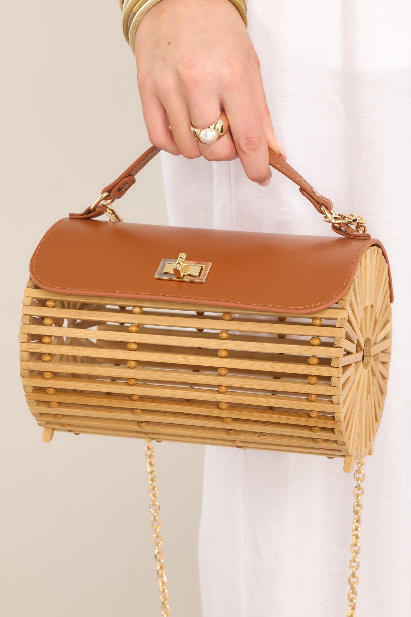 Close up view of this bamboo handbag that features a top handle, a single flap design, a twist lock closure, and a removable chain strap.