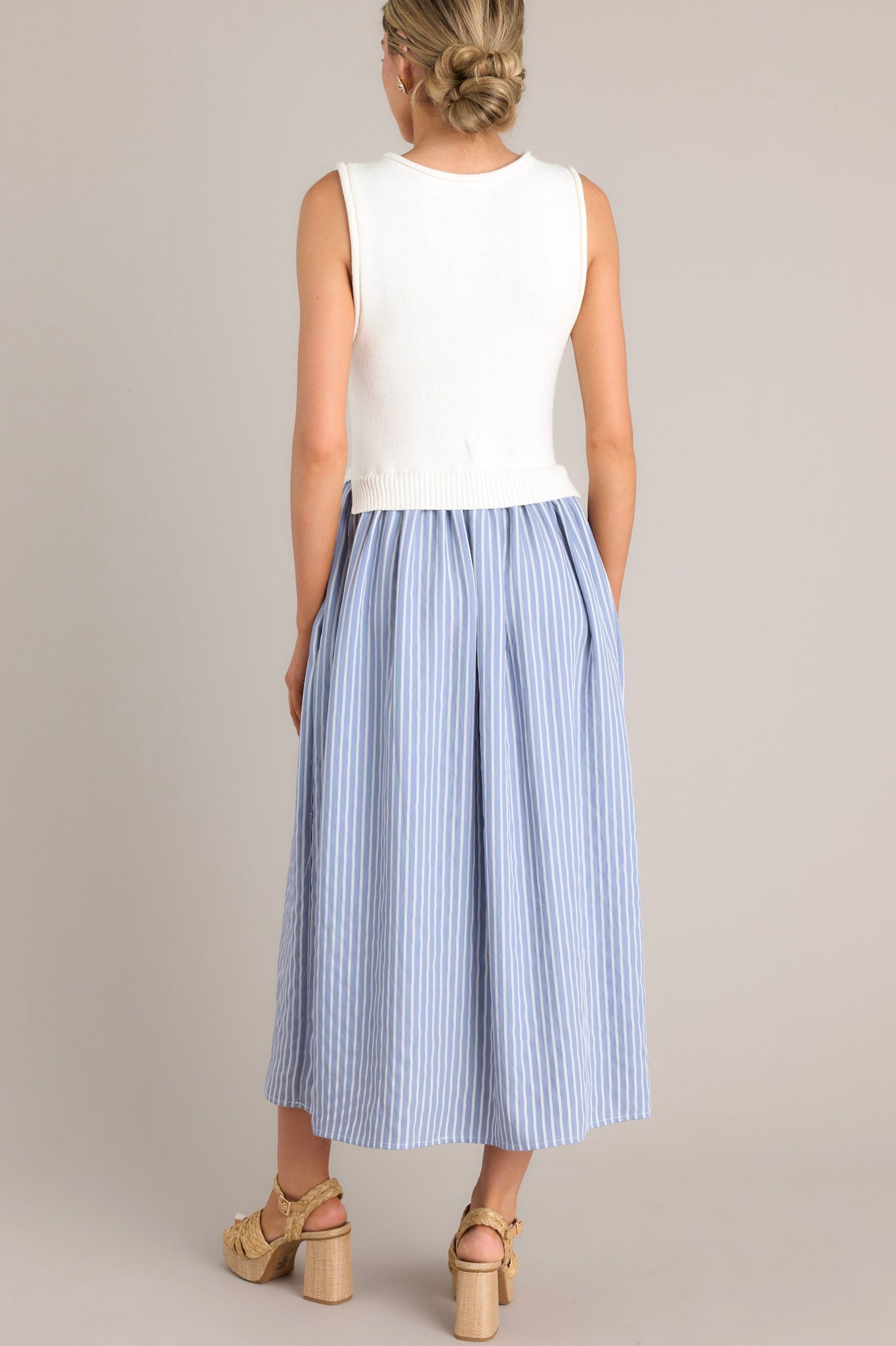 Back view of a blue striped dress highlighting the high neck design, sleeveless bodice, and overall fit.