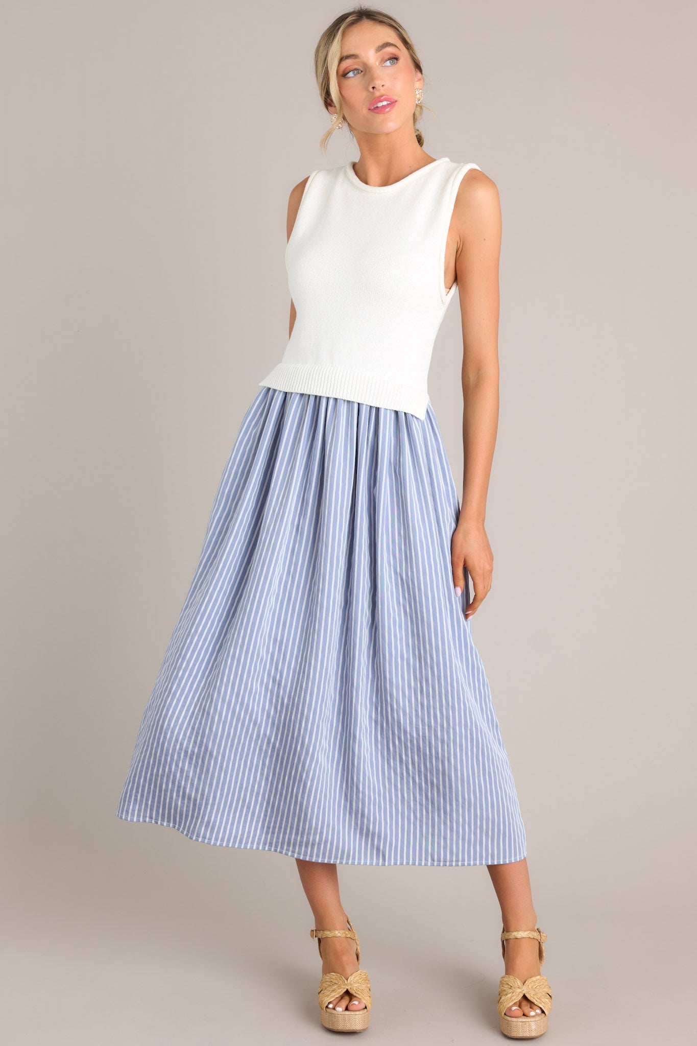 Front angled view of a blue striped dress featuring a high neck design, a knit sleeveless bodice, functional pockets, and a single tiered flowy skirt