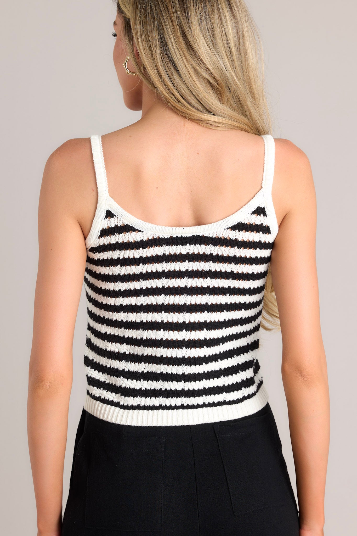 Back view of a black stripe tank featuring thin straps, a striped pattern, a lightweight knit material, and a slightly cropped hemline.