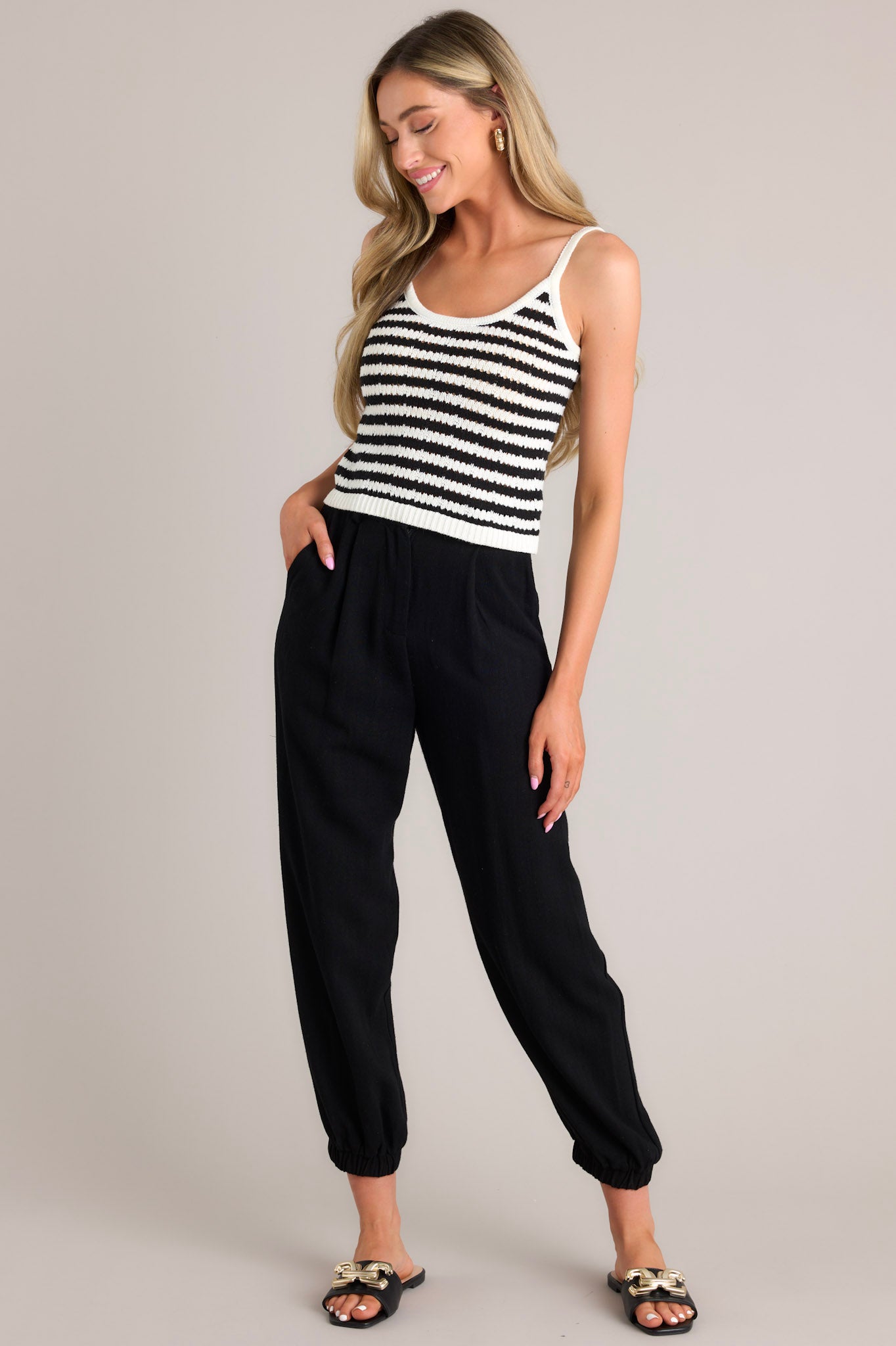 Angled Full length view of a black stripe tank featuring a scoop neckline, thin straps, a striped pattern, a lightweight knit material, and a slightly cropped hemline
