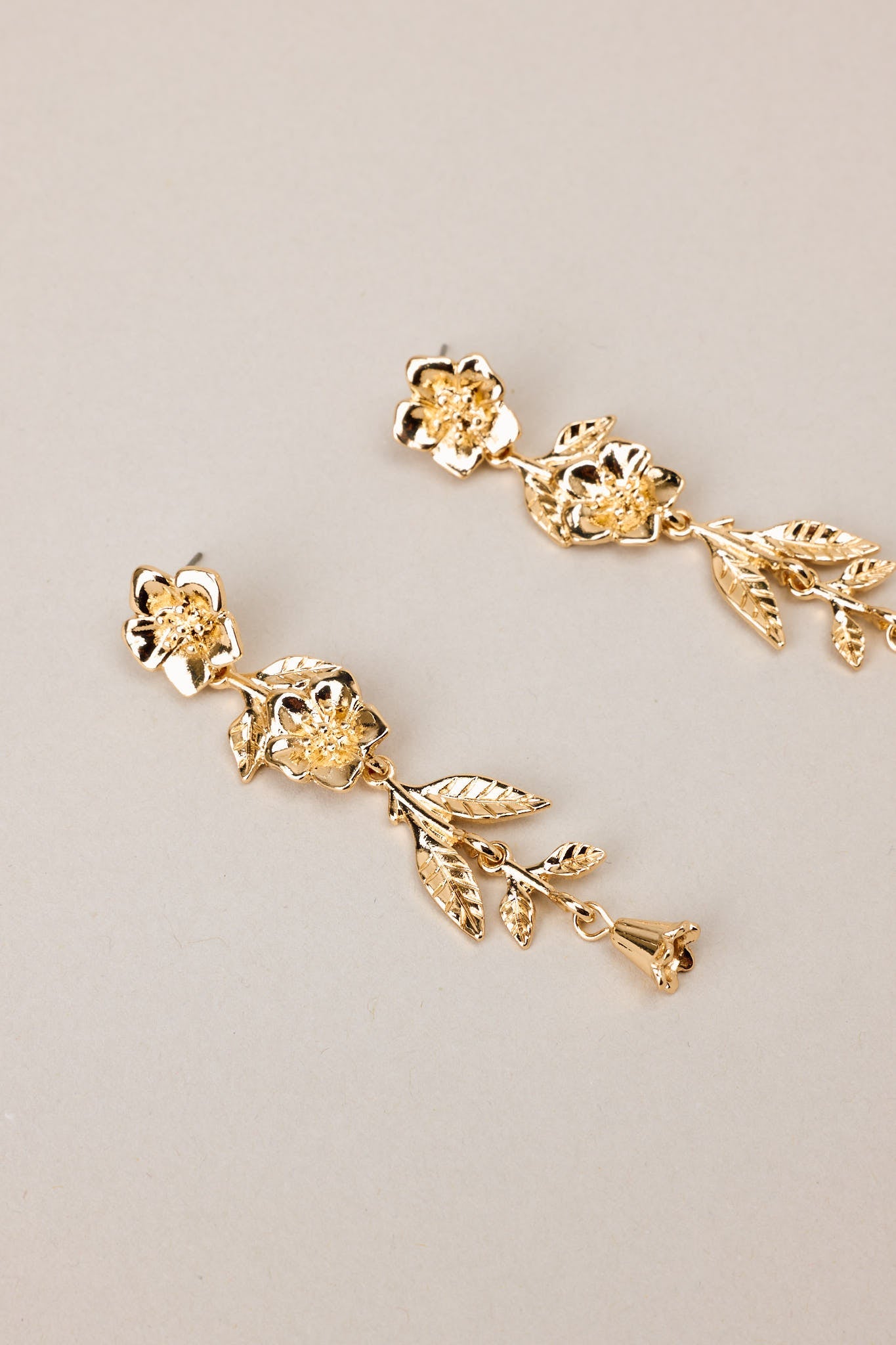 Angled overhead view of these gold floral earrings that feature gold hardware, a flower shaped stud, and secure post backings.