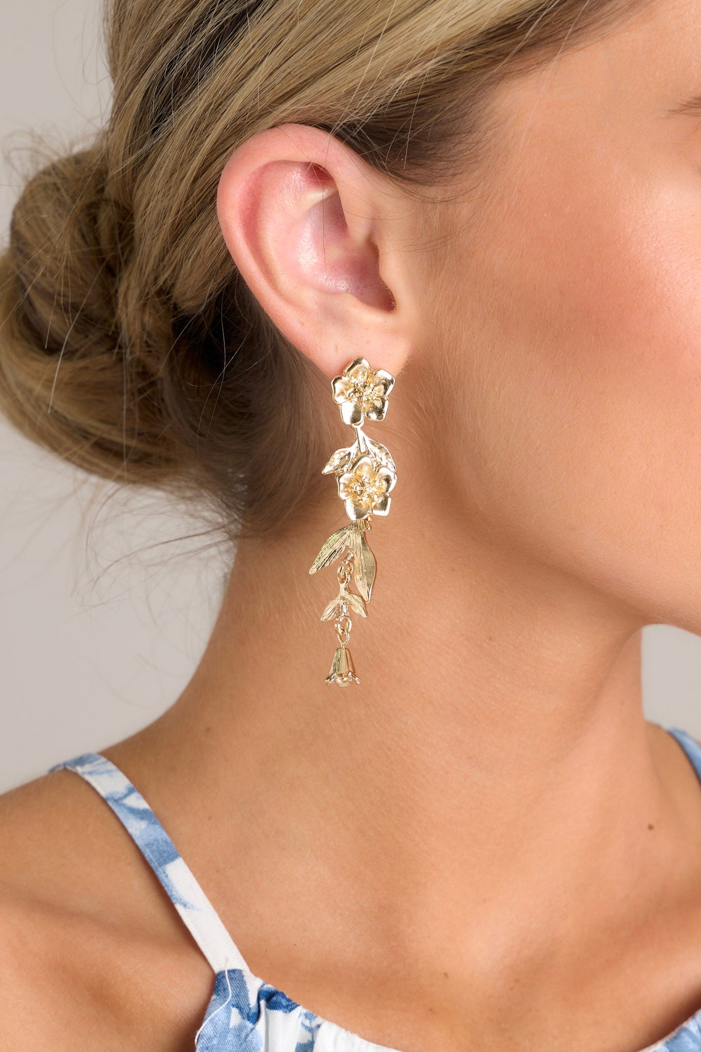 Close up view of these gold floral earrings that feature gold hardware, a flower shaped stud, and secure post backings.