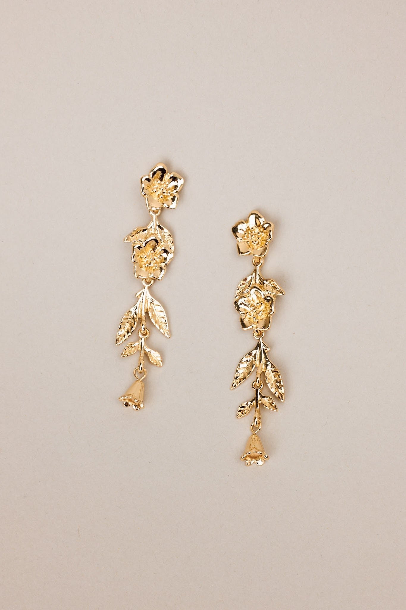 Overhead view of these gold floral earrings that feature gold hardware, a flower shaped stud, and secure post backings.