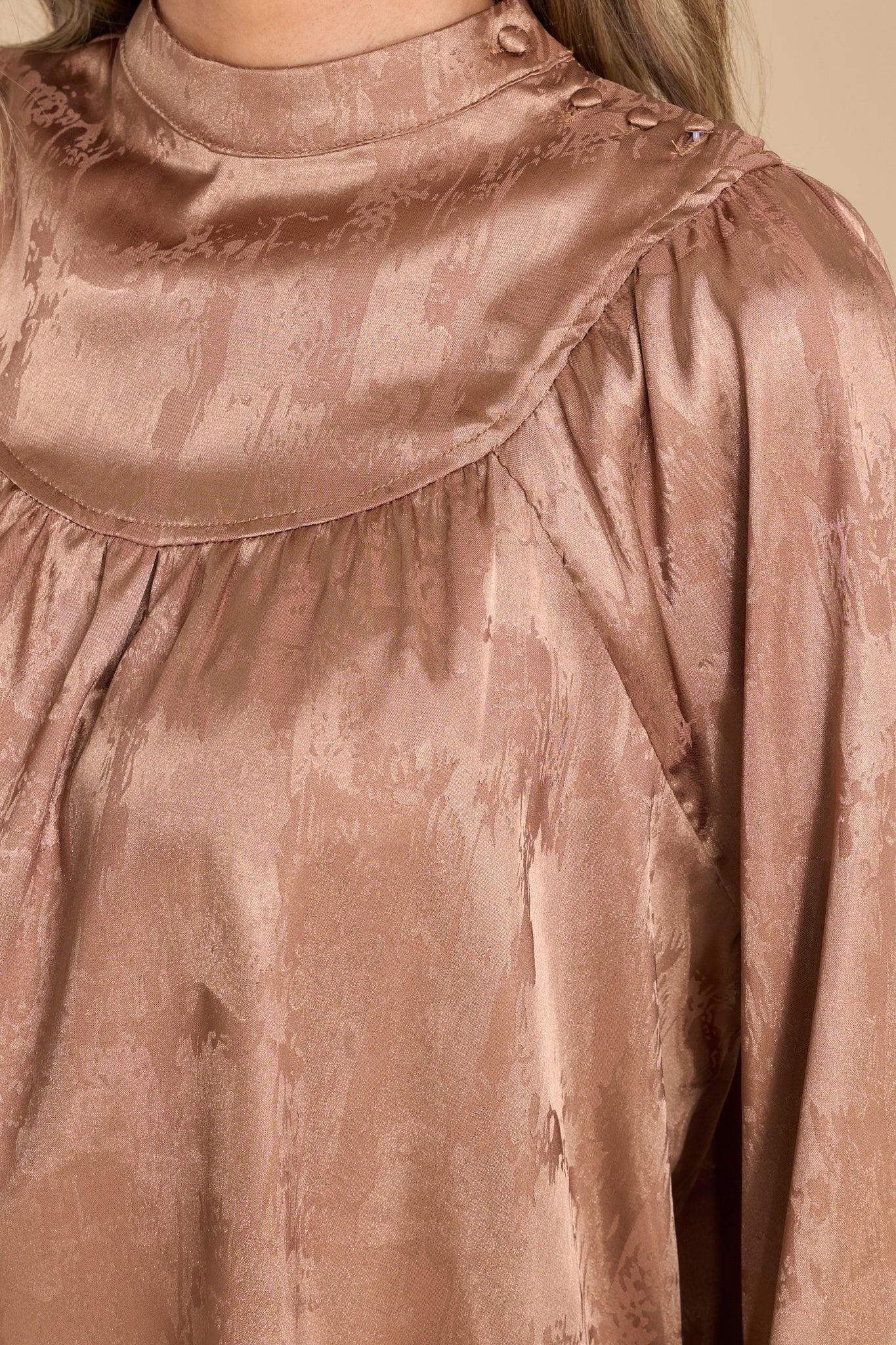 Close up view of this shiny satin-like top that features a high neckline with buttons trailing down on top of the shoulder.