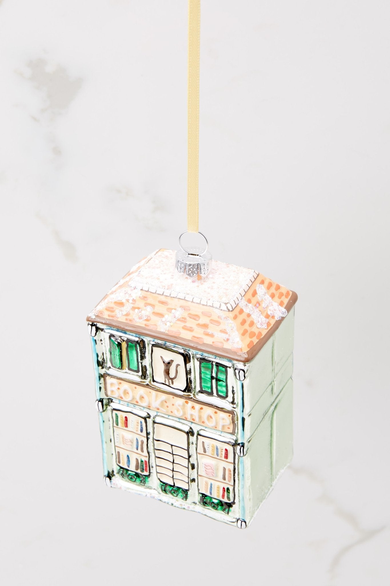 Top view of this ornament that features a building shape that says "BOOK SHOP" and has a cat in one of the windows.