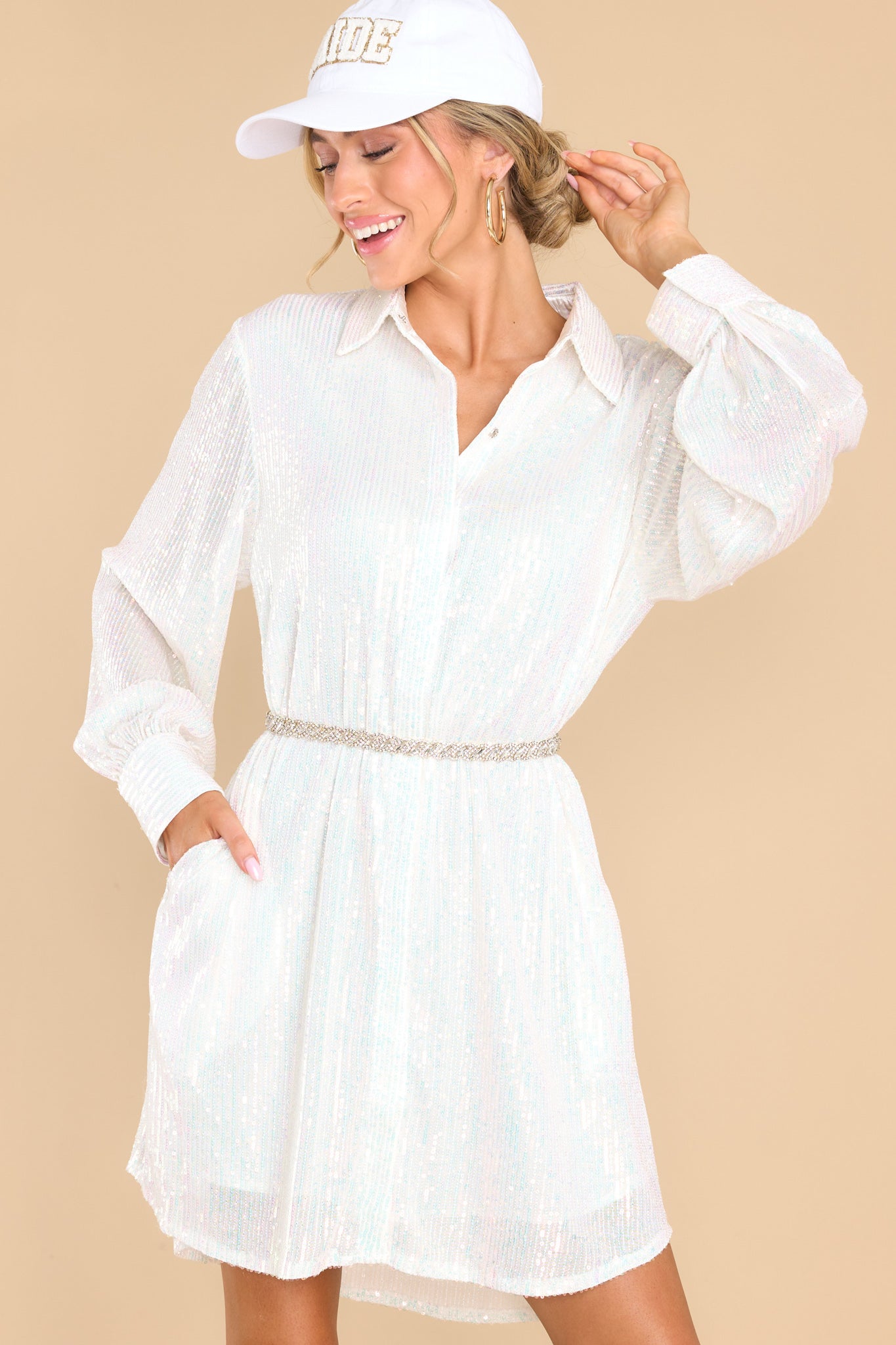 This all white dress features a collared neckline, functional buttons down the front, sheer long sleeves, and sequin embellishments throughout.