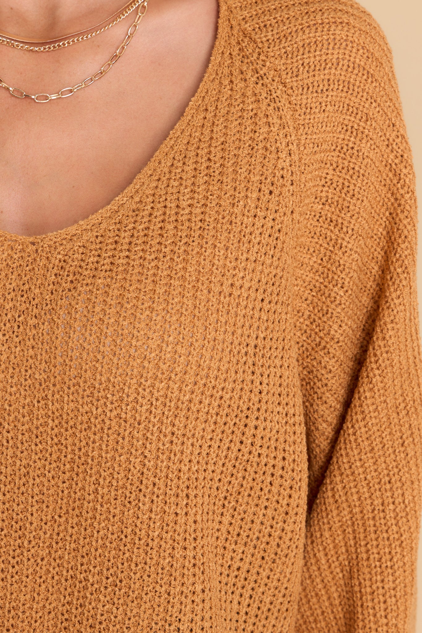 Close up view of this sweater that features a subtle v-neckline, long sleeves with tapered cuffs, a bottom hem that is approximately 2" longer in the back, and a knit texture throughout.