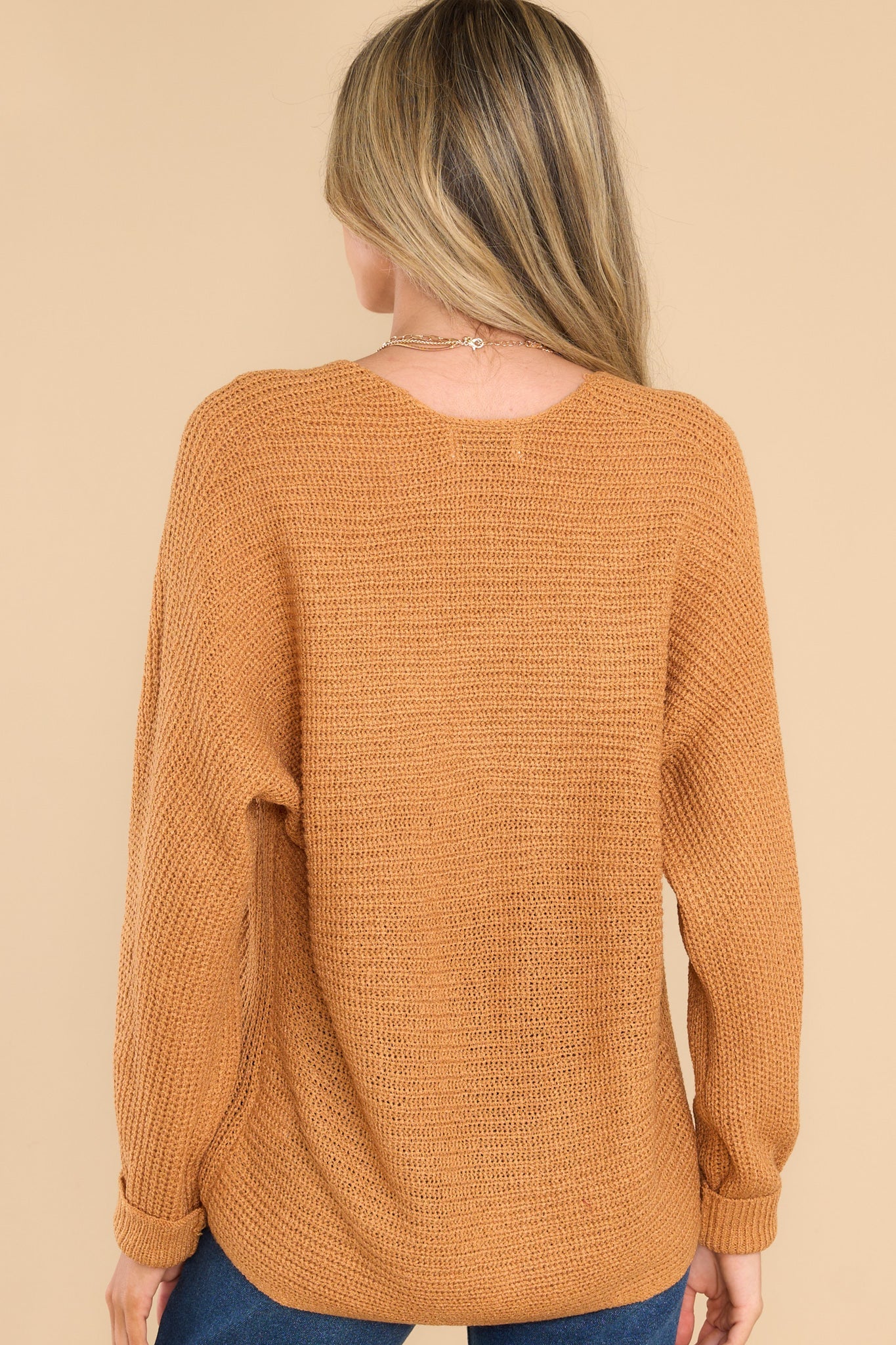 Back view of  this sweater that features a subtle v-neckline, long sleeves with tapered cuffs, a bottom hem that is approximately 2" longer in the back, and a knit texture throughout.