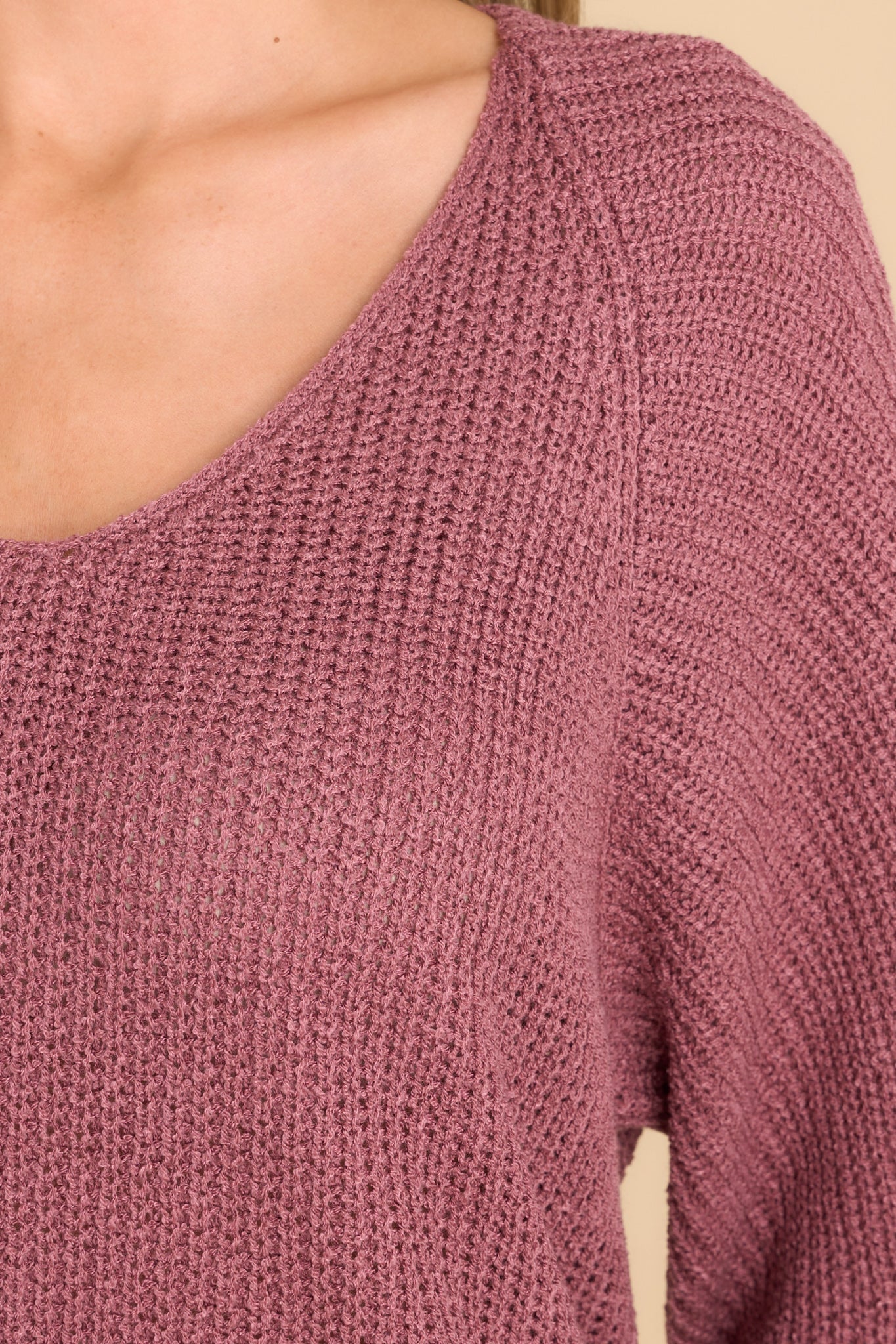 Close up view of this sweater that features a subtle v-neckline, long sleeves with tapered cuffs, a bottom hem that is approximately 2" longer in the back, and a knit texture throughout.