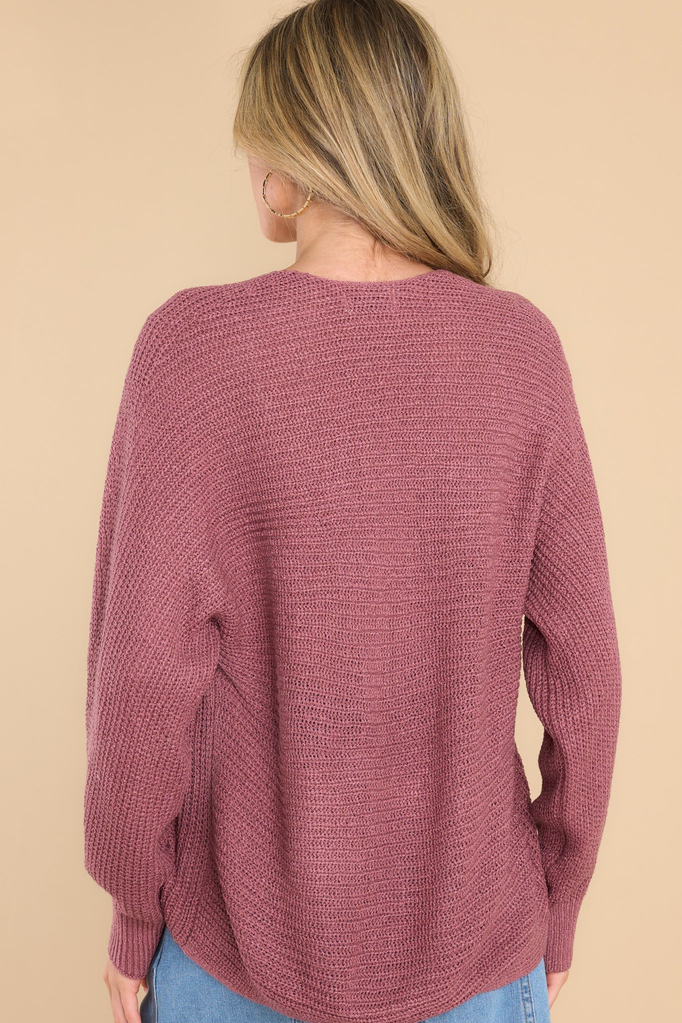 Back view of this sweater that features a subtle v-neckline, long sleeves with tapered cuffs, a bottom hem that is approximately 2" longer in the back, and a knit texture throughout.