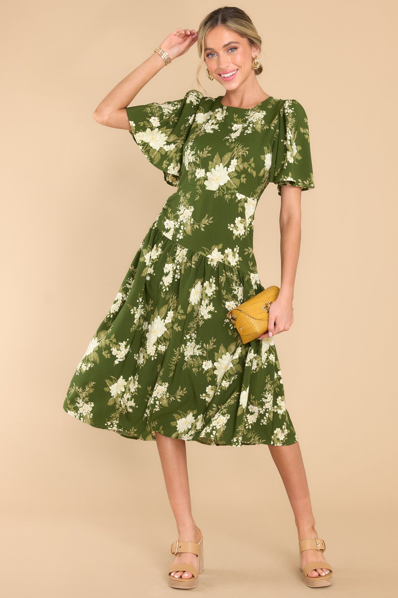 This green dress features a round neckline, butterfly sleeves, a keyhole cutout at the back of the neck with a button closure, a side zipper, and an asymmetrical detail along the waistline and hips.