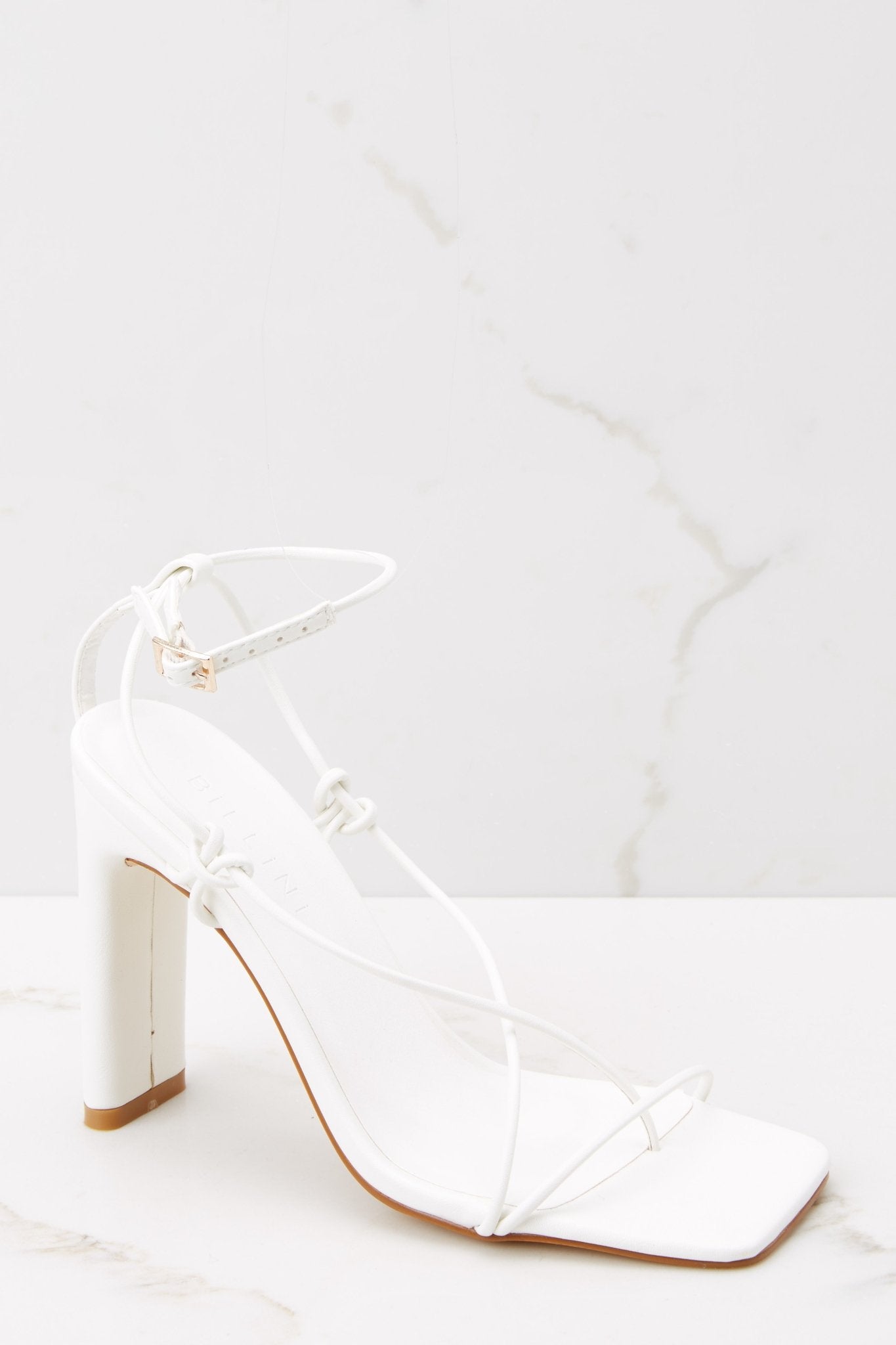 Outer-side view of these heels that feature thin straps that cross up the feet to buckle in at the ankle, a square tow, and thin straight heels.