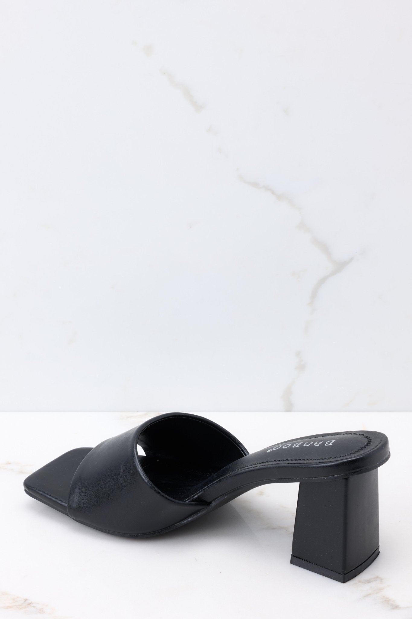 Inner-side view of these heels that feature a square toe, a thick strap across the top of the foot, a square heel, a faux-leather finish, and a slip-on design.