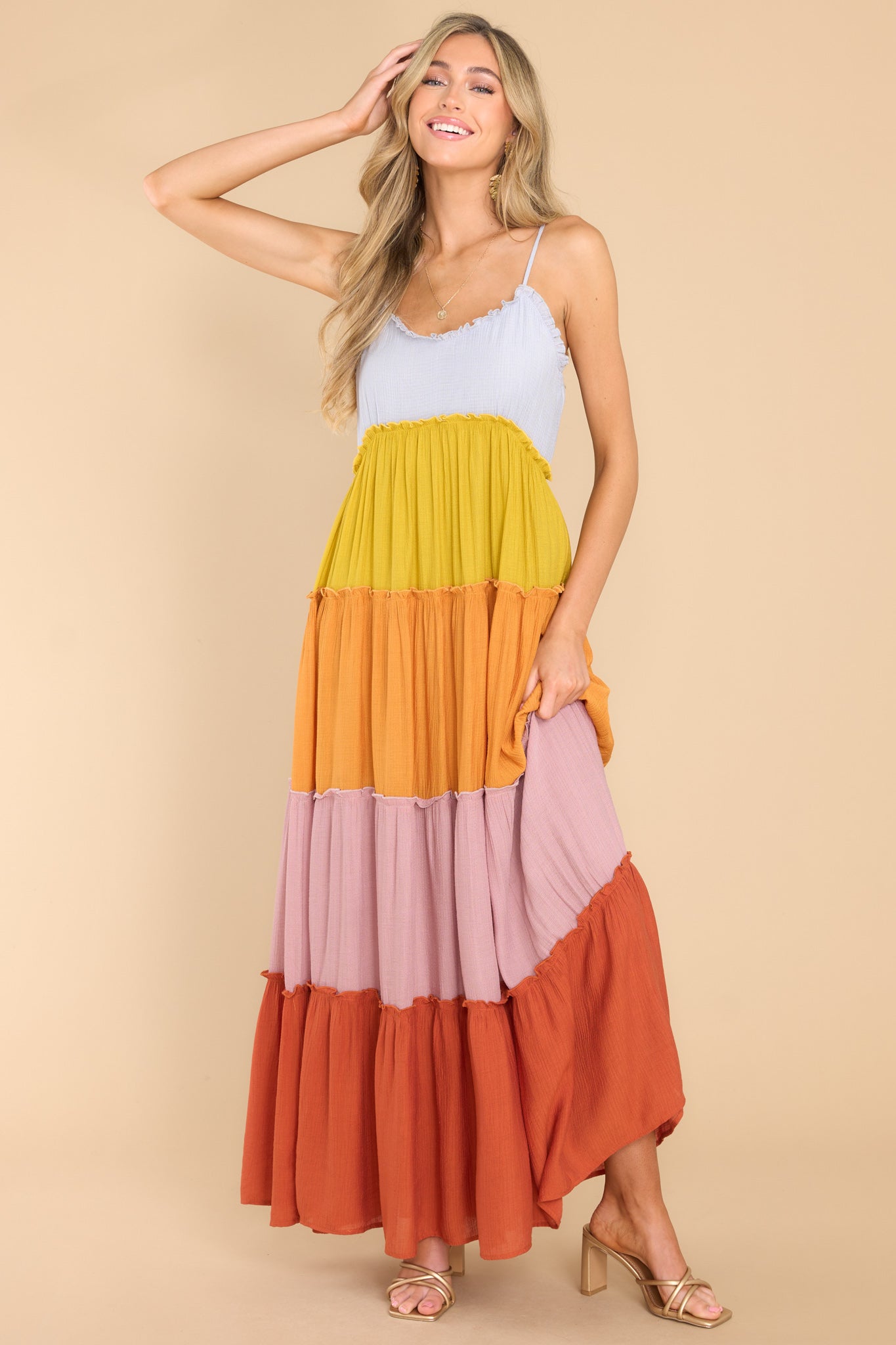 Full body view of this dress that features a sweetheart neckline with ruffle detailing, thin adjustable shoulder straps, functional buttons for closure in the back of the bust, and a multicolored, tiered skirt with ruffle detailing.