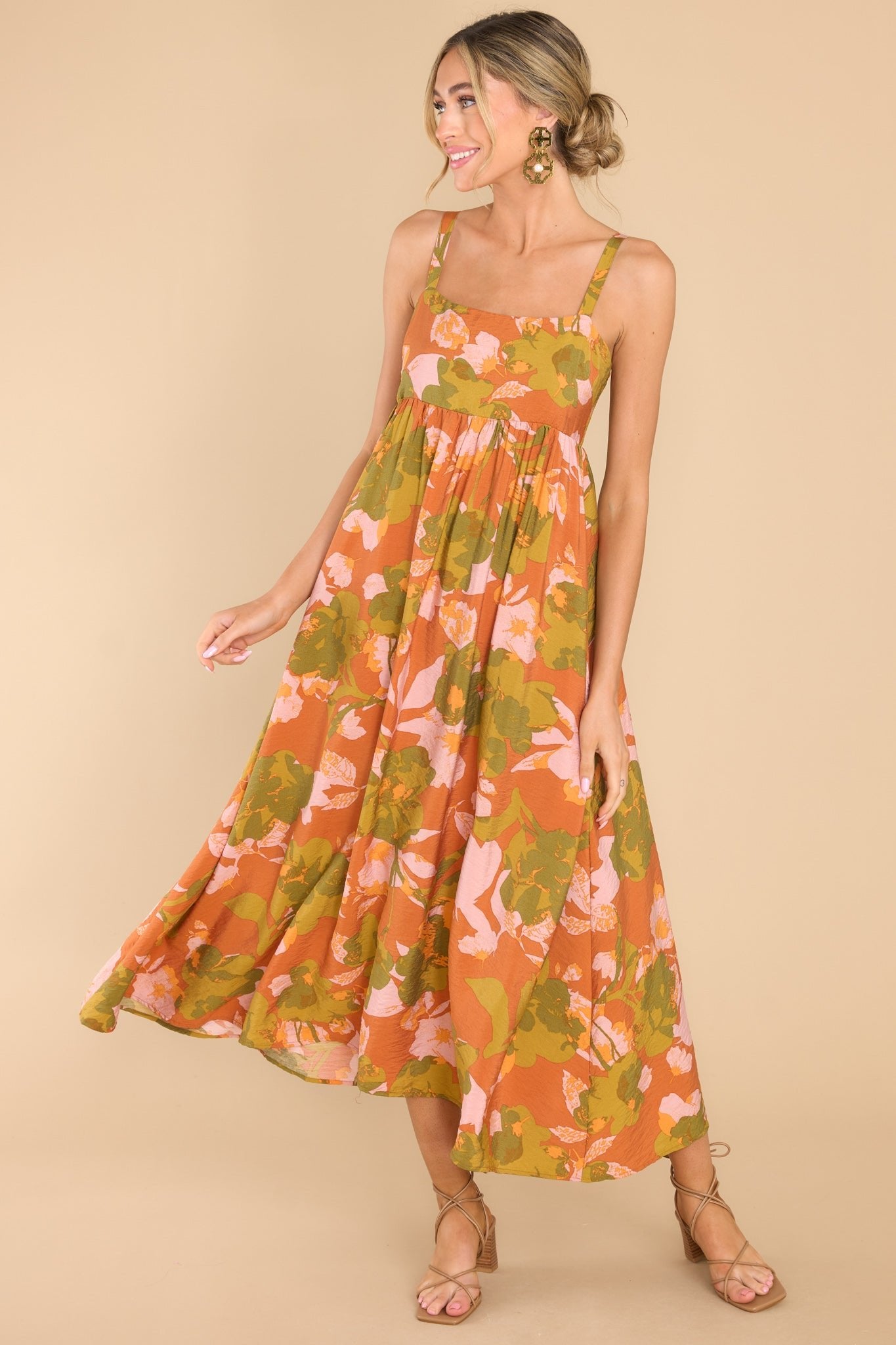 This orange and green dress features a square neckline, thin adjustable shoulder straps, a babydoll silhouette, a smocked section in the back of the bodice, and a flowy skirt.