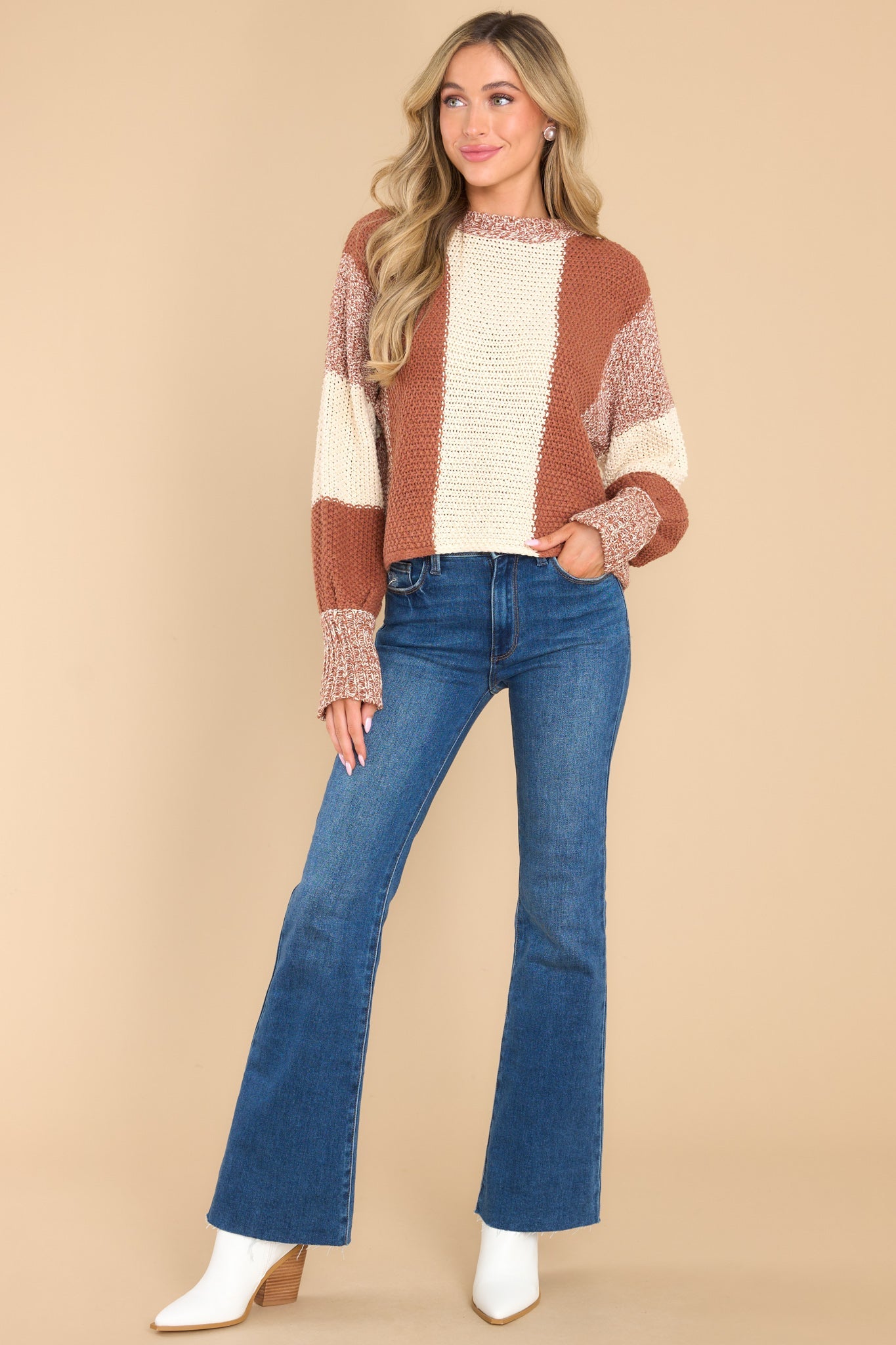 This ivory and orange sweater features a round neckline, long sleeves with stretchy cuffs, a chunky knit texture, and a striped colorblock design.