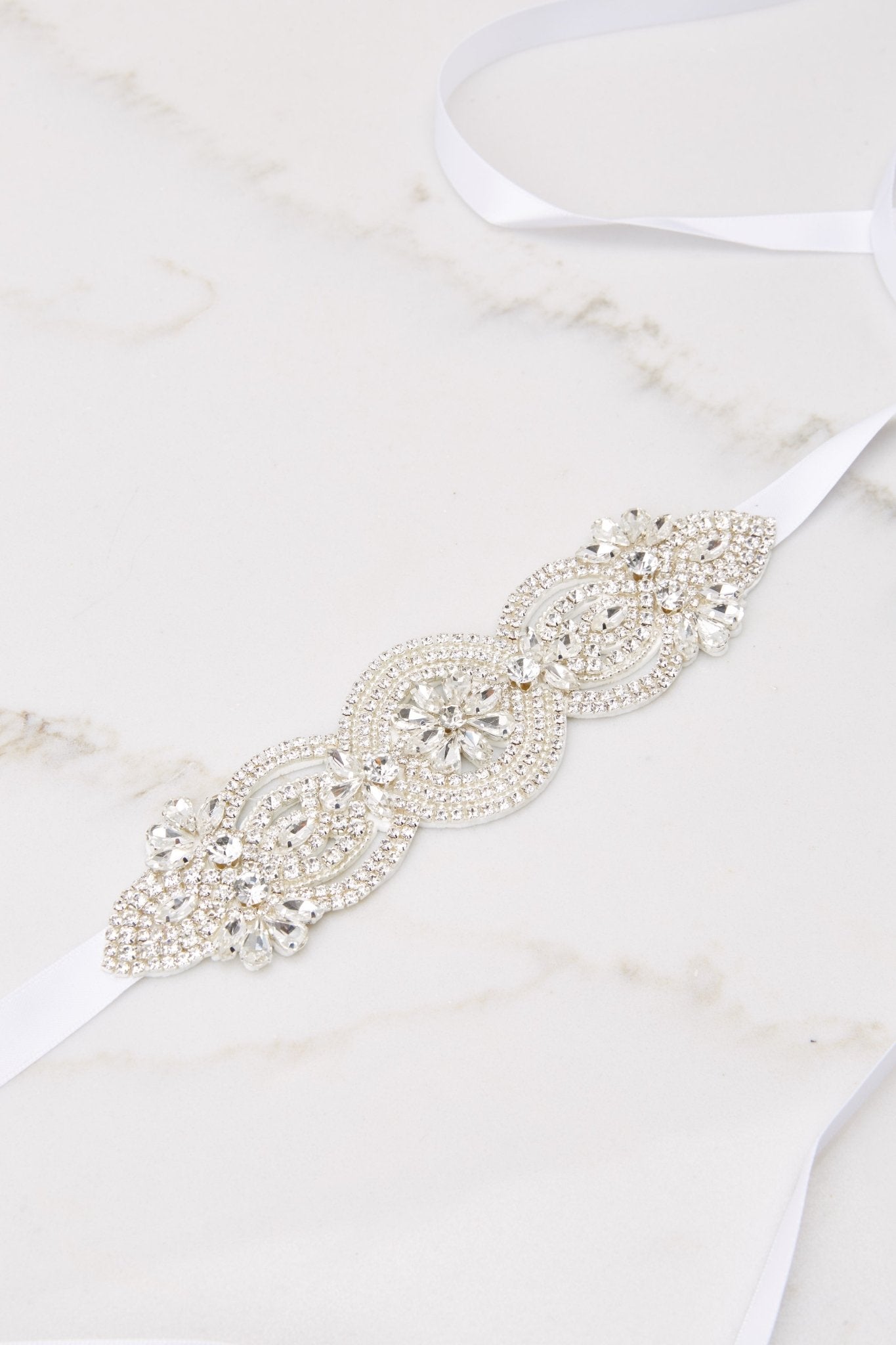 Close up view of this belt that features a crystal centerpiece with floral details, and a self-tie ribbon closure.