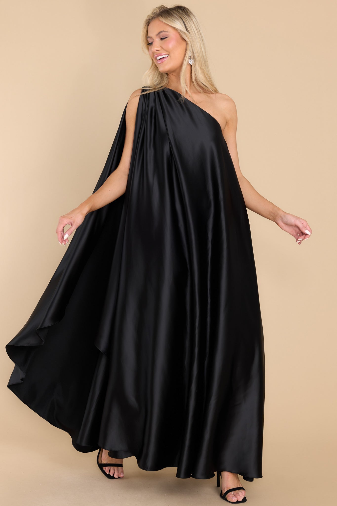 This all black dress features a hidden one shoulder design, scoop neckline, and open sleeves.