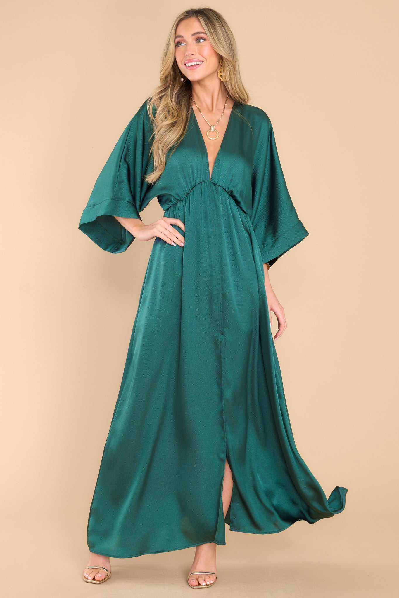 Front view of this dress that features a plunging v-neckline, dolman sleeves, an elastic waistband, a flowy skirt with a slit up the center, and a lining that extends from the waist to the thigh.