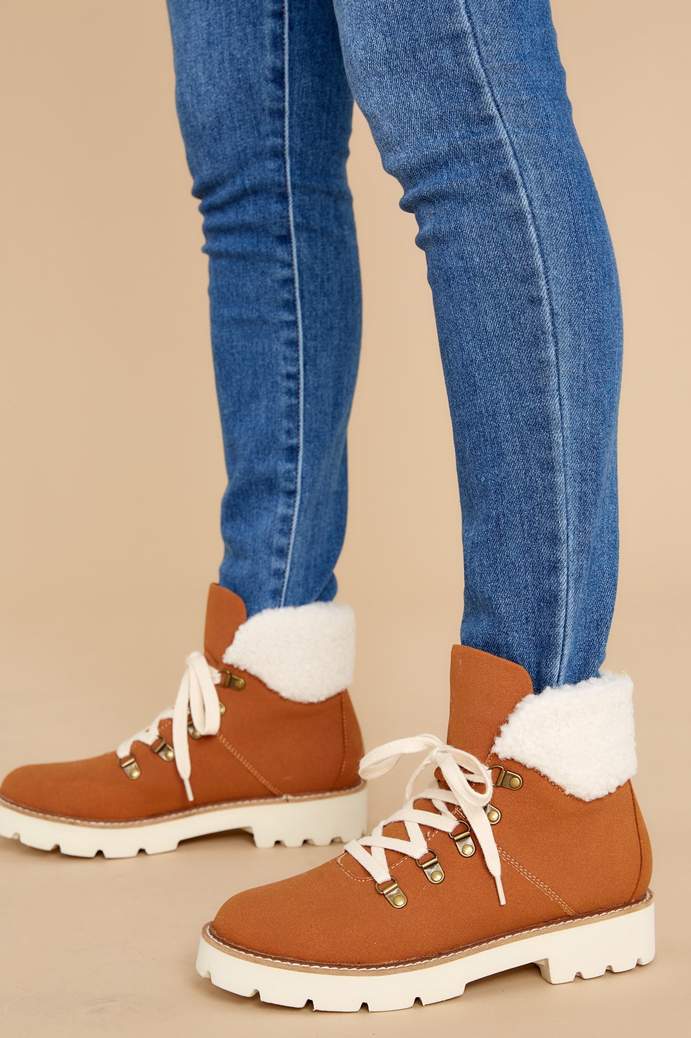 Close up view of these boots that feature white faux fur around the ankle, an ivory chunky sole and ivory laces up the front.