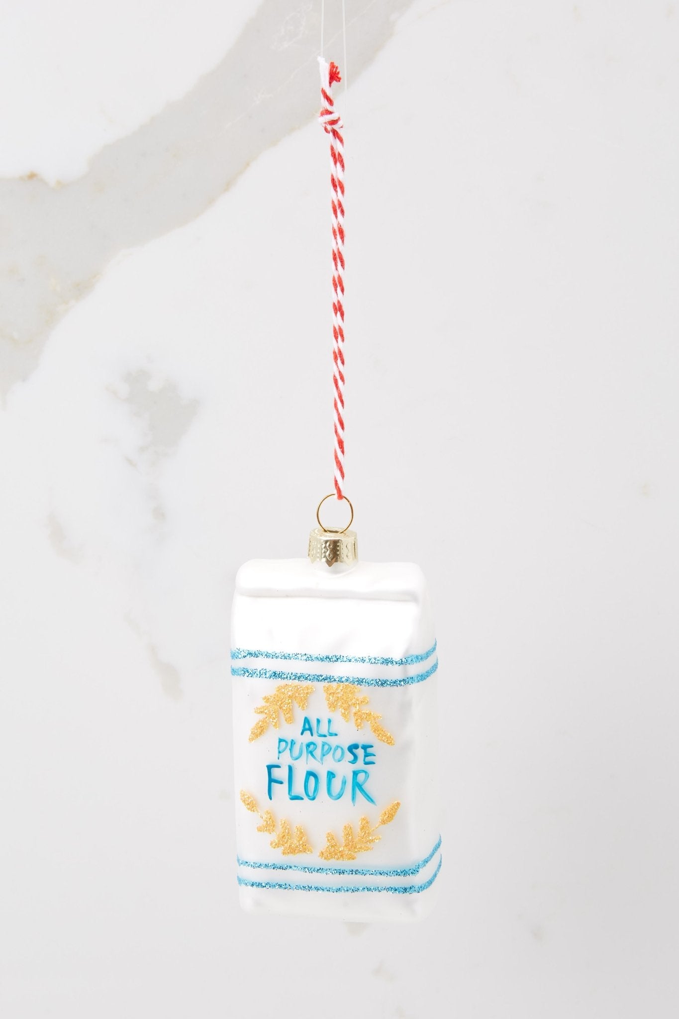 This white ornament features a design of 'all purpose' flour with hand painted blue lettering and gold glitter accents.