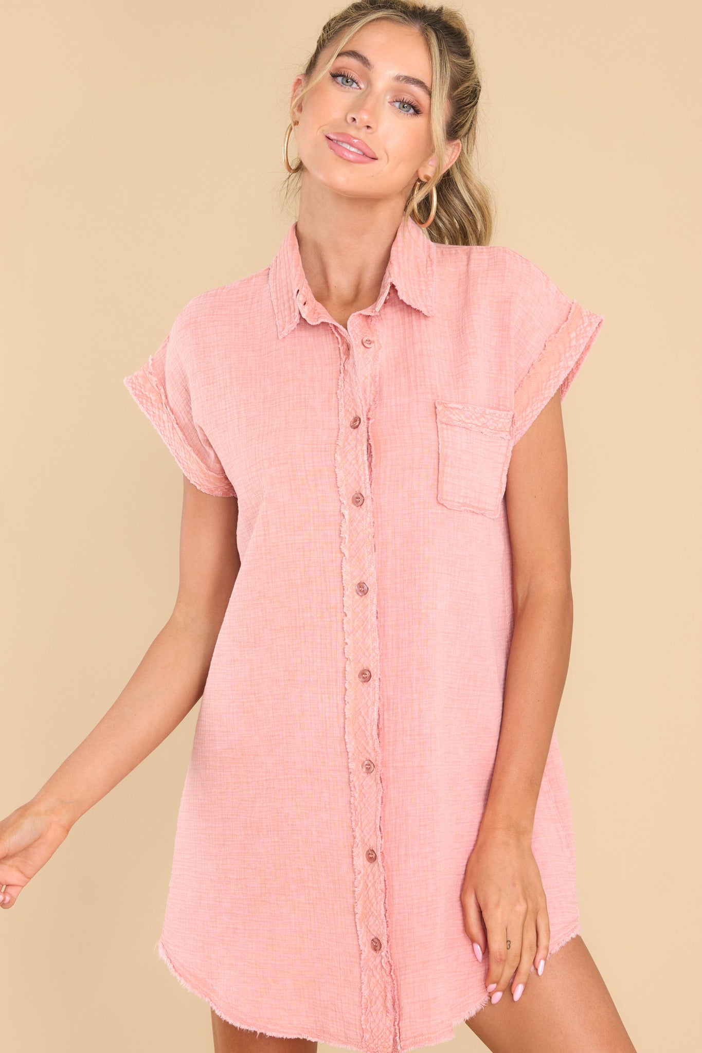 This pink dress features a collared neckline, functional buttons down the front, one functional bust pocket, and distressed hem detailing.