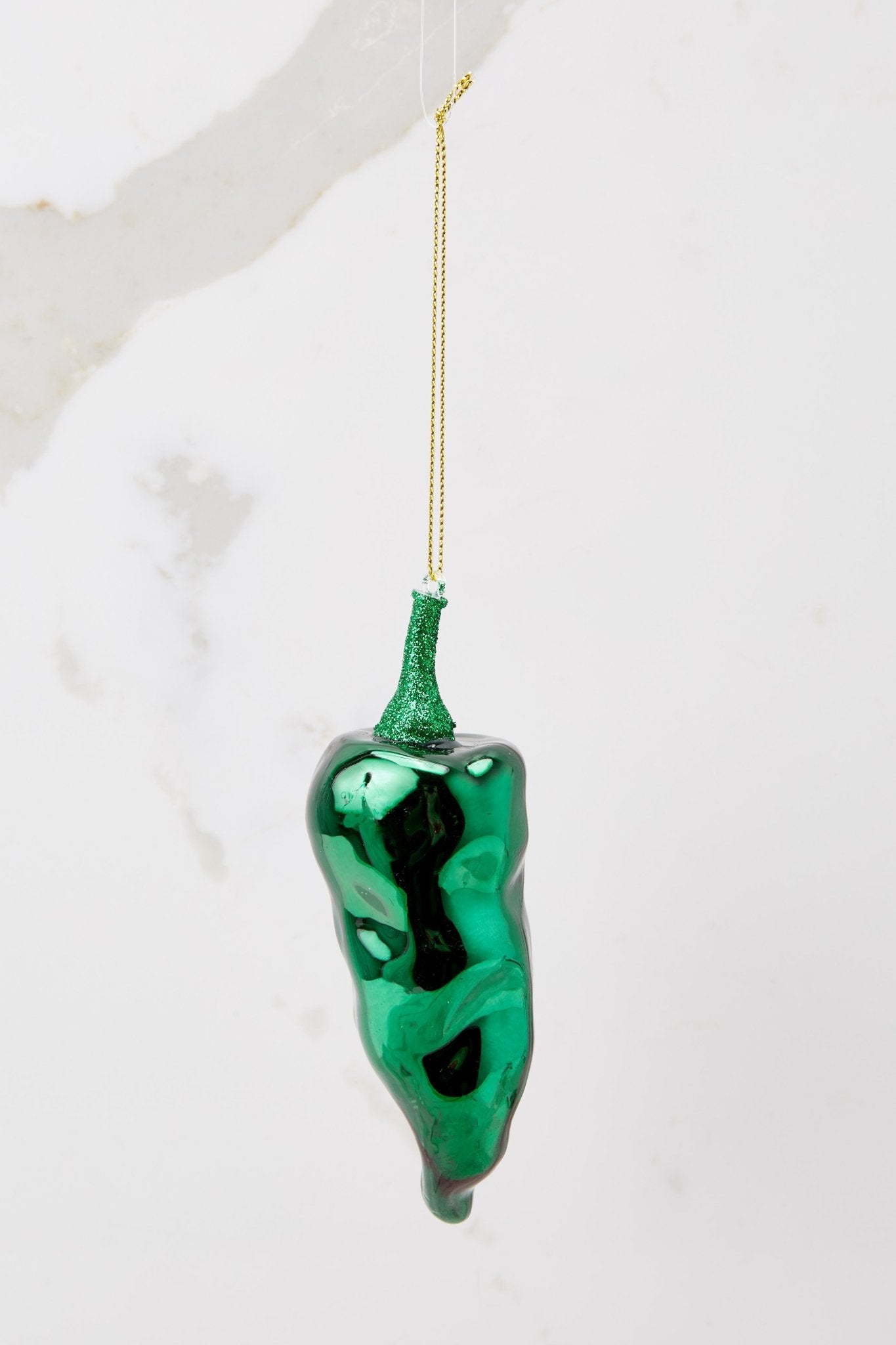 This green ornament features a design of pepper with green glitter detailing and a gold string.