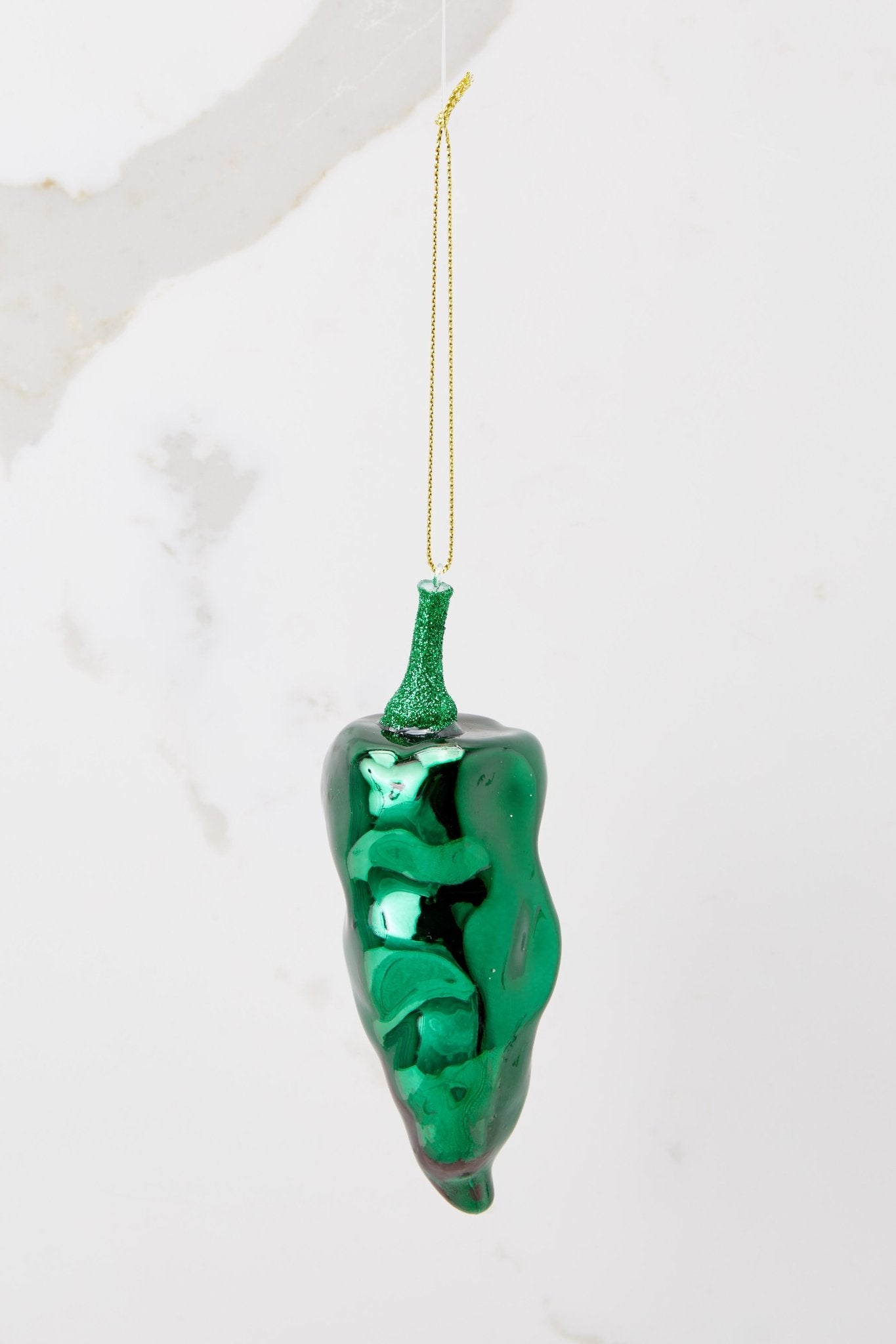 Close up view of this ornament that features a design of pepper with green glitter detailing and a gold string.