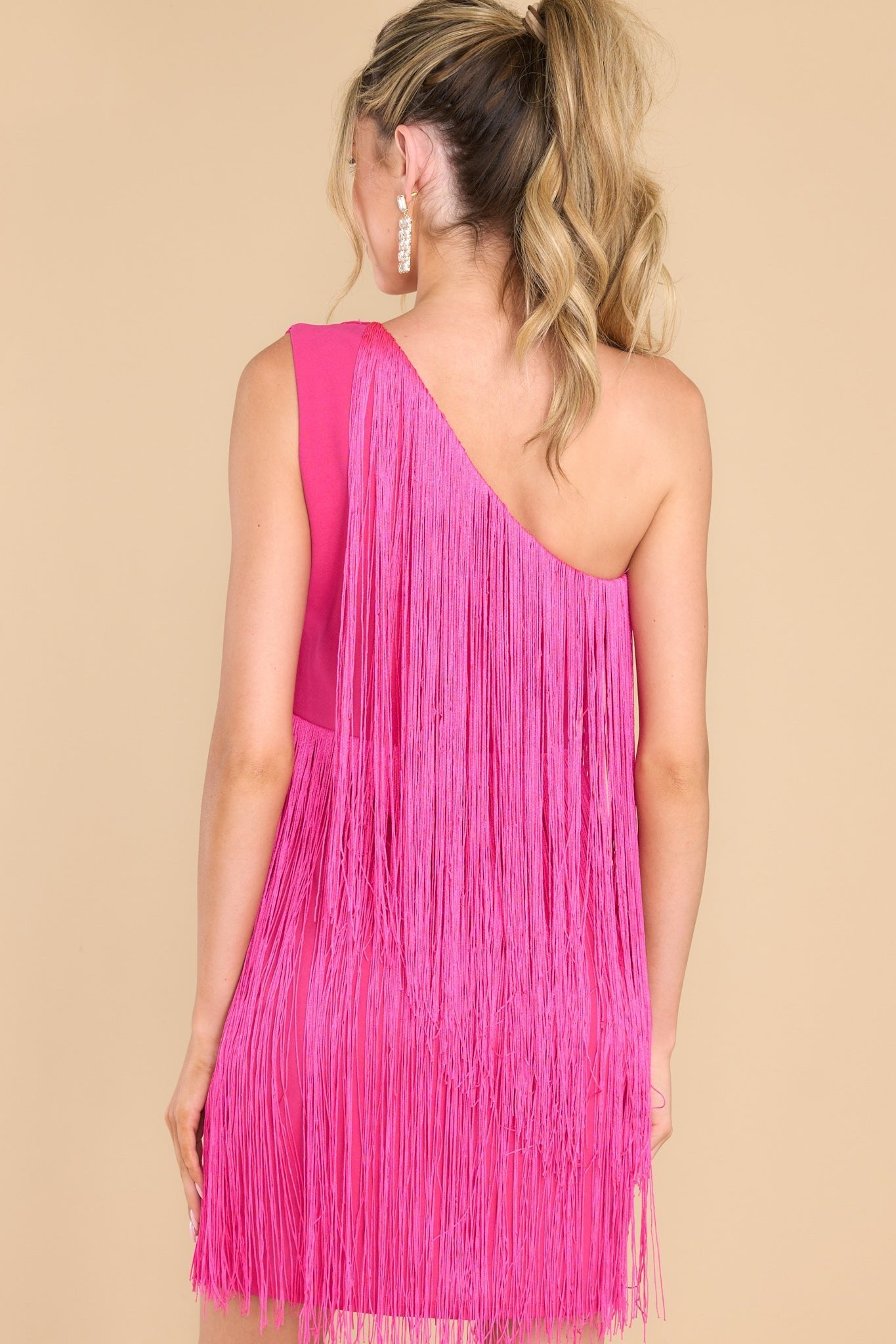 Back view of this dress that features a one shoulder design, functional zipper on the side, and fringe detailing throughout with lots of movement.