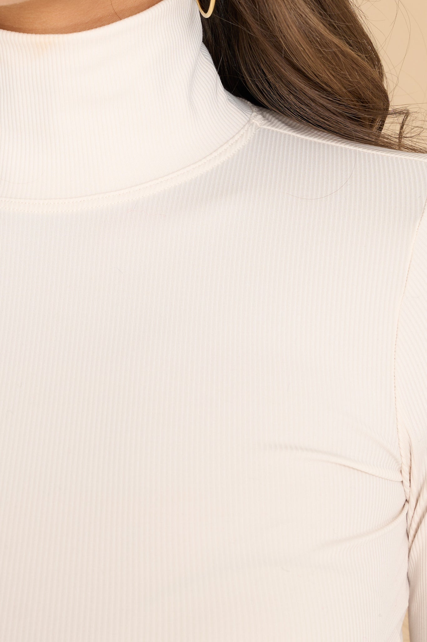 Close up view of this bodysuit that features a turtleneck design, long sleeves, a ribbed texture throughout, and thong-style bottom with a snap button closure. 