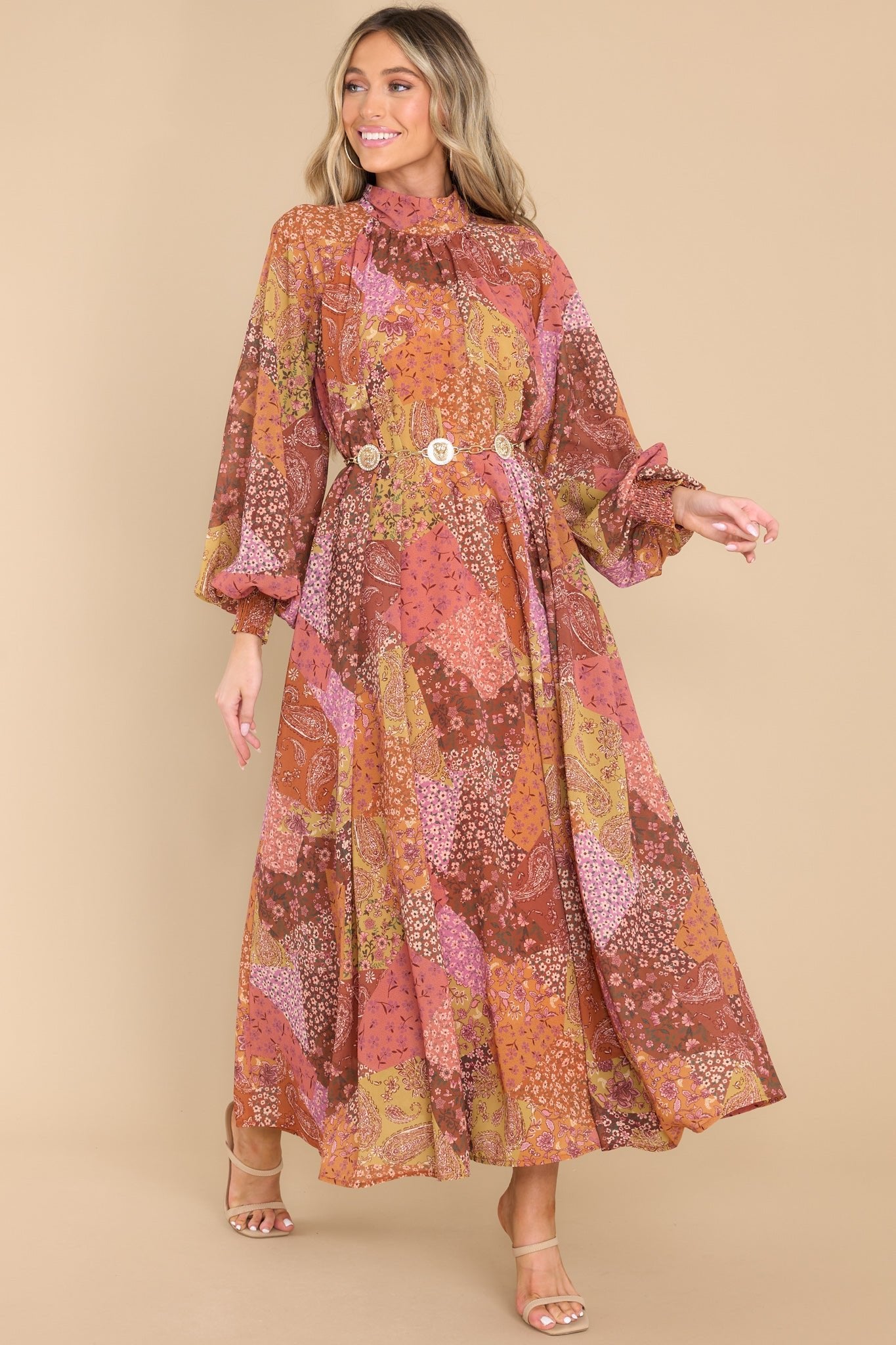This rust colored multi print dress features a high neckline with long-sleeves, and a self tie behind the neck.