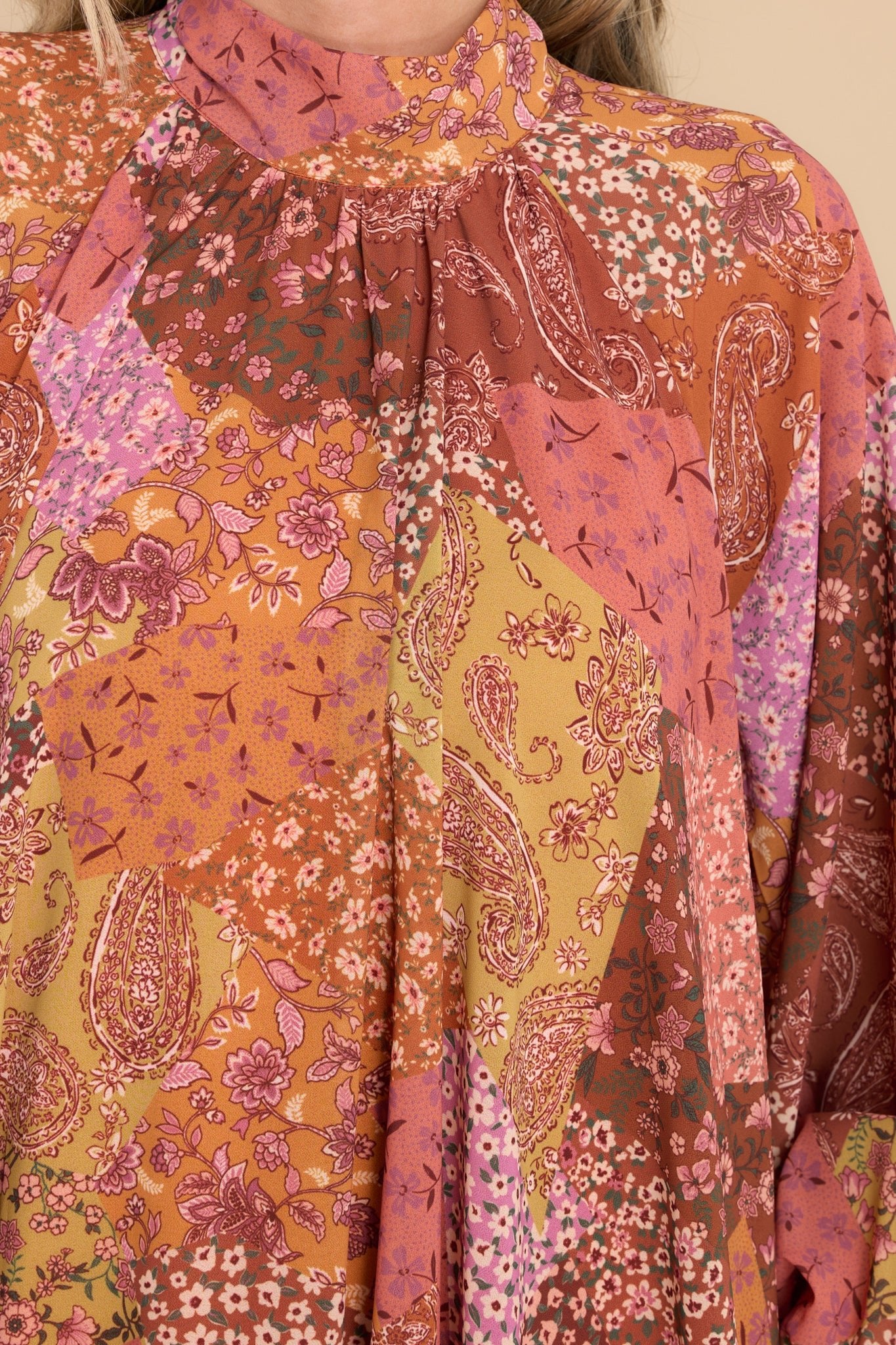 Close up view of this multi print dress that features a high neckline with long-sleeves, and a self tie behind the neck.