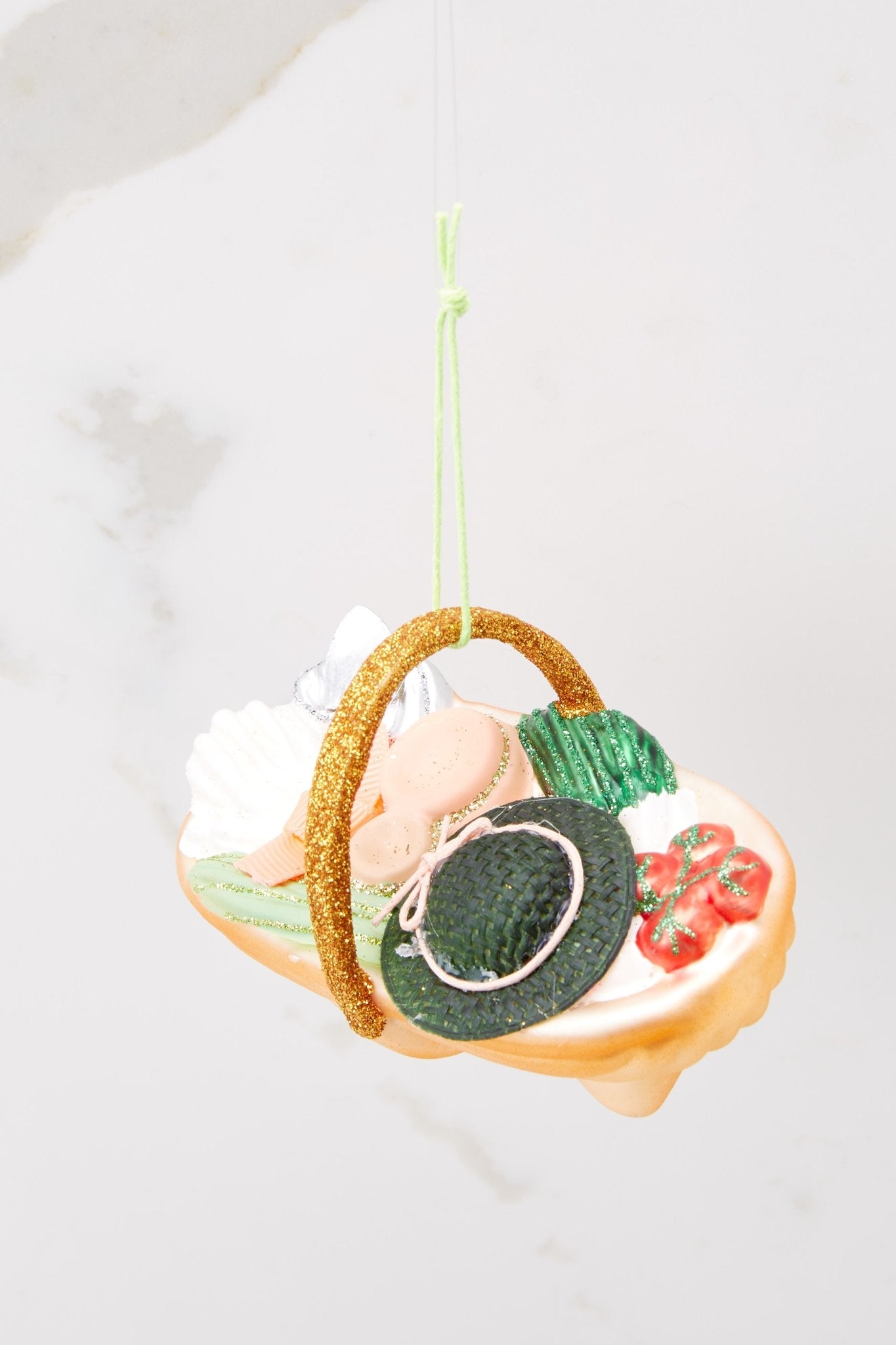 Top view of this ornament that features a glittered design of a market basket filled with a shovel, gloves, tomatoes, and green leafy vegetables. 